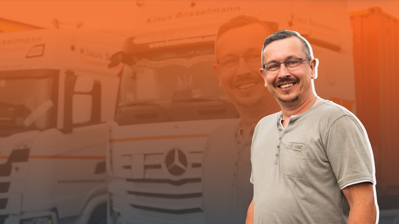 Ein lächelnder Mann mit Brille und T-Shirt steht vor einem LKW mit Mercedes-Stern und dem Text "Klaus Wassermann".