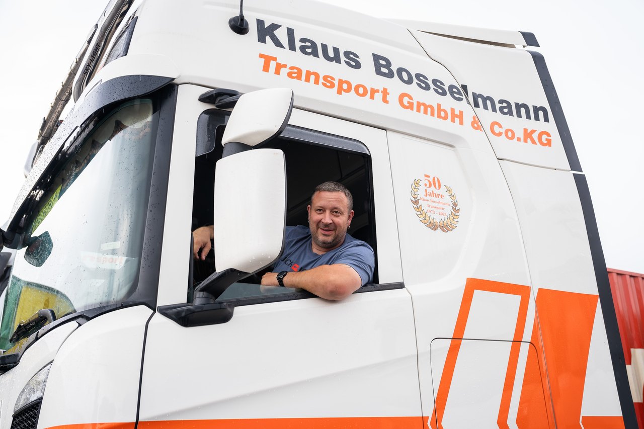 Ein lächelnder LKW-Fahrer schaut aus dem Fenster eines weißen Klaus Bosselmann Transport Lastwagens.