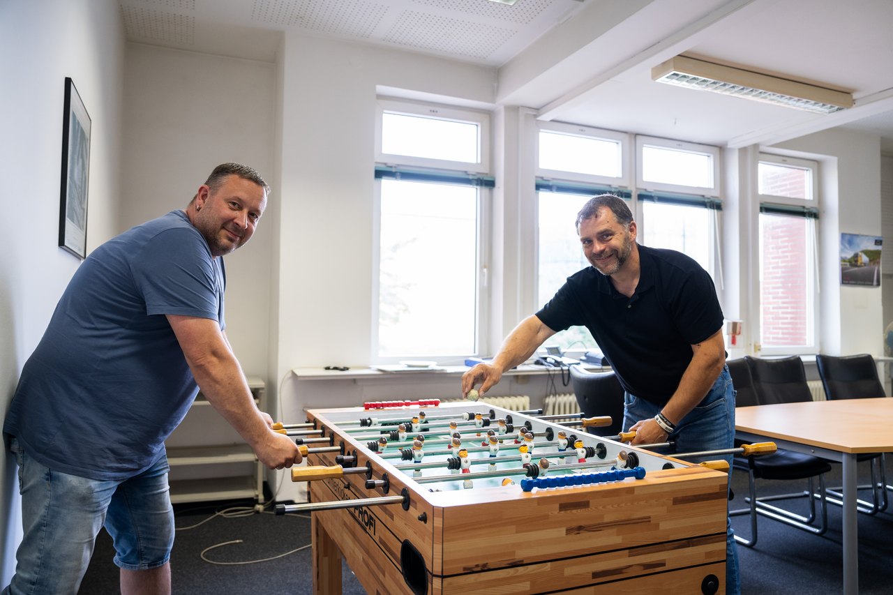 Zwei Männer lächeln, während sie an einem Tischfußballtisch in einem Büro spielen.